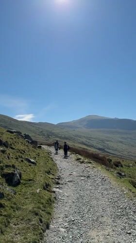 Hikers traverse mountain path in Llanberis under clear skies