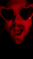 Man performs in red heart sunglasses under red lighting