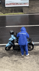 Pulling over in the rain to suit up on a light blue scooter