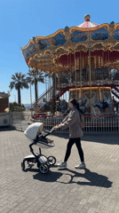 Woman with stroller enjoys morning walk past Sochi carousel