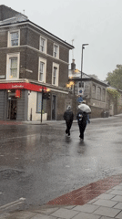 Two pedestrians cross London street during morning rain