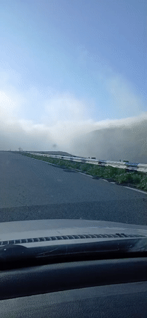 Vehicle drives mountain road in foggy conditions early morning