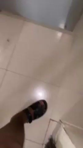 A person is walking on a light-colored tile floor. The person is wearing black sandals. The video is shot from a high angle, looking down at the person's feet. The person is moving forward. The background is blurry, but appears to be a wall and a door.  The lighting is bright.