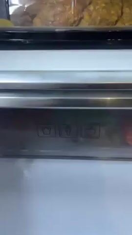 A stainless steel refrigerator drawer is opened, revealing a container of "Tender Top Baby Carrots," Brussels sprouts, and red and orange bell peppers. Above the drawer is a compartment that appears to hold fried food.  The drawer has small icons of a bell pepper, carrot, and tomato on the front.