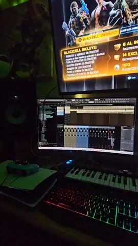 The media file captures a dimly lit home office or creative workspace, likely at night, in Alto Hospicio, Chile. The central focus is a multi-screen computer setup. A large TV screen, mounted above, displays an in-game offer for "BLACKCELL" priced at "29.99USD," detailing various "BlackCell" inclusions like operator skins, blueprints, and "1100 Puntos COD instantáneos." Text like "MEJOR OFERTA" and "PASE DE BATALLA" indicates a gaming context, likely Call of Duty.

Below the TV, two computer monitors are visible. The left monitor shows a Digital Audio Workstation (DAW) software, featuring waveforms, mixer channels, and other music production elements, suggesting active audio editing or creation. The right monitor displays another application, partially obscured, with a prominent "TUTO" graphic.

On the desk below the monitors, a gaming keyboard with vibrant RGB backlighting (red, orange, green, blue zones) is present. To its left, a MIDI keyboard controller with blue and purple illuminated pads and keys suggests music production capabilities. A computer mouse on a mousepad is visible to the right of the keyboard. On the far left of the desk, a small blue gamepad or controller rests on a white piece of paper or notebook, near a partially visible speaker. Green accent lighting emanates from behind the TV or from LED strips on the wall, adding to the ambient glow of the screens. No people are visible in the frame.