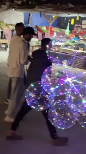 Evening street scene features person with illuminated balloons in Gaza