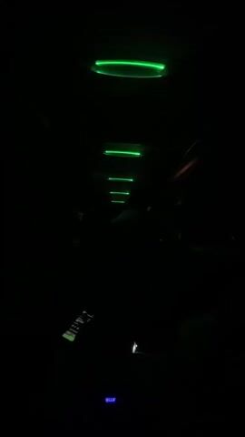 The video shows the interior of a vehicle, likely a van or bus, at night. Green LED strip lights are illuminating the ceiling in evenly spaced intervals. A small, rectangular electronic device with buttons is visible in the foreground.  A small display is illuminated with the word "BLUE".  Loud, pulsing music plays in the background.