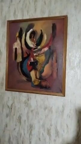 Here's a description of the video:

The video shows a framed abstract painting hanging on a textured wall. The painting features various colors and shapes, including black, white, yellow, red, and blue, set against a brownish-purple background. It appears to be an oil painting with thick brushstrokes. The frame is simple and made of wood. The wall has a textured pattern, possibly wallpaper. The camera zooms in slightly on the painting.