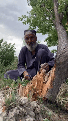 Elderly man sits in rural field under cloudy skies