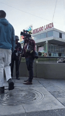 Man walks toward Mercado Lanza square as cameramen document scene