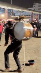 Street drummer performs for crowd wearing harness-mounted bass drum