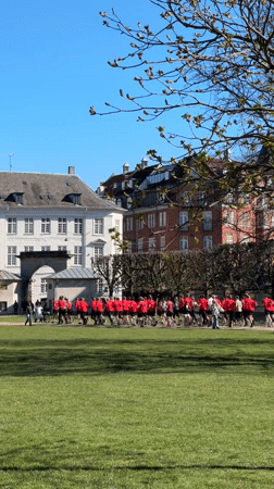 Teenagers in red shirts run through Copenhagen park near castle
