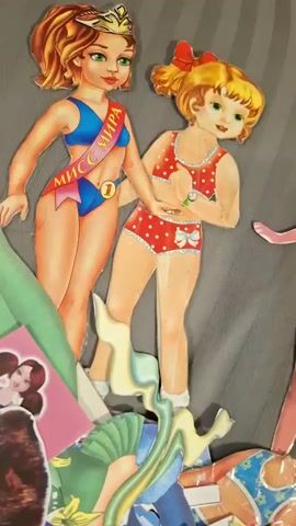 The video shows several paper dolls and their clothes spread out on a grey surface. The dolls appear to be vintage, with cartoon-like features and brightly colored swimsuits. One doll wears a sash that says "Мисс Мира," which translates to "Miss World."  The clothes are also colorful, with various dresses, outfits, and accessories scattered around the dolls. The dolls and clothes appear to be made of paper or cardstock. The camera pans over the dolls and clothes, showing them from different angles. There is no visible background besides the gray surface.