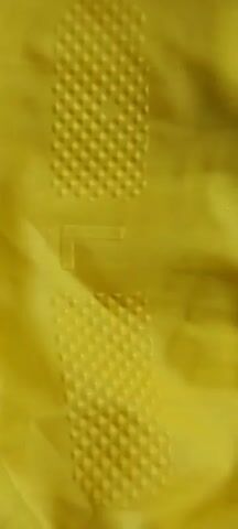 The video shows two pairs of blue and yellow rubber gloves on a white surface. The gloves are laid out in a crisscross pattern. The camera zooms in on the gloves, revealing the textured grip on the palms and fingers. The gloves appear to be new and unused.