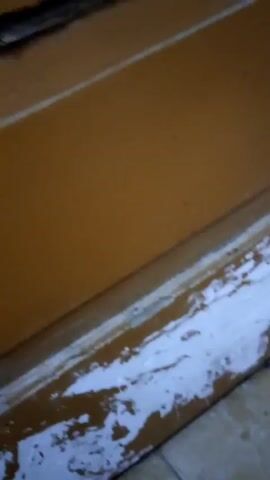 The video shows a close-up view of a wooden door. The door has multiple panels, some of which appear to be stained or painted a light brown color. There is a door handle on the left side of the door. The lighting in the video is dim and the image quality is poor, making it difficult to discern finer details. The door appears to be in a residential or commercial setting, but the specific environment is unclear. There are no people visible in the video. The actions depicted are limited to the camera slowly panning across the surface of the door.