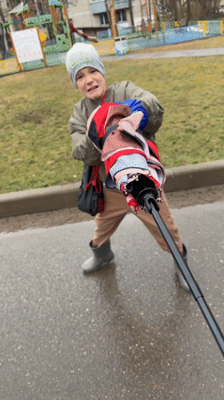 Boy plays with umbrellas on wet walkway in Dmitrov