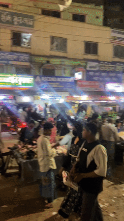 Nighttime street activity captured in Dhaka's illuminated commercial district