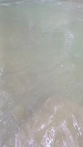 The video shows a close-up, overhead view of a body of water, likely a river or stream. The water is murky and appears to be flowing, with some ripples and small waves visible. The bottom of the body of water is visible in places, revealing rocks or sediment beneath the surface. The lighting suggests it is daytime, and the overall impression is one of a natural outdoor environment. There are no people or man-made objects clearly visible in the frame.
