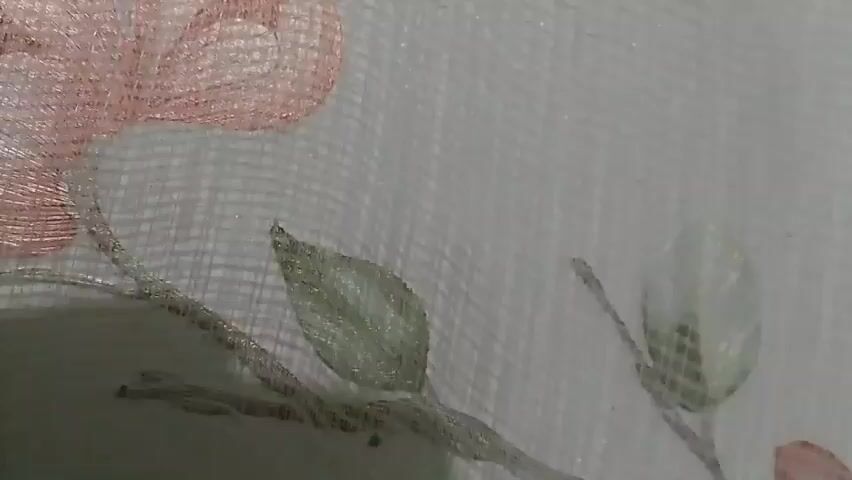 The video displays a close-up, panning shot of a sheer fabric with an embroidered floral pattern. The embroidery features pink flowers and green leaves, creating a delicate design. The fabric itself has a textured weave, visible as fine vertical lines throughout the image. The lighting appears to be soft and natural, illuminating the details of the embroidery and the fabric's texture.