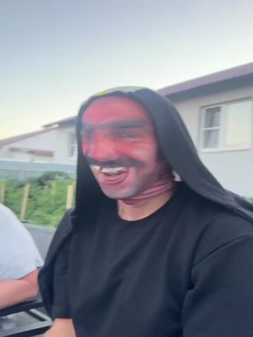 This video shows several people outdoors in what appears to be a backyard. In the first clip, a person wearing a red mask with a mustache and a black hooded sweatshirt is visible. In the second and third clips, another person wearing a mask resembling a hockey mask is seated, with another person in a black jacket standing behind them, laughing. In the final two clips, a person is shown wearing a mask with a distorted facial expression, and two young girls are visible in the background near a trampoline. The environment suggests a casual gathering or party.