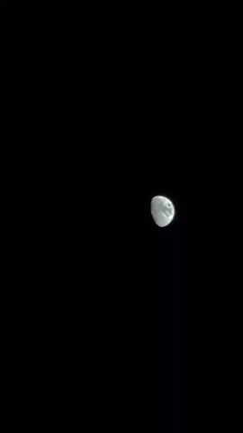 This is a video of the moon in the night sky. The moon is partially illuminated, showing its craters and surface details. The sky is completely dark, indicating it is nighttime. The video is shot from a stationary position, allowing the moon to appear to move slightly across the frame due to Earth's rotation. No people, objects, text, or specific location cues are visible beyond the moon itself. The time of day is clearly night, and no weather conditions are discernible. The overall mood is serene and contemplative, typical of observing the night sky.