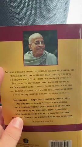 The video shows a person holding and displaying the book "The King of Knowledge," a translation of a work by A.C. Bhaktivedanta Swami Prabhupada. The person first shows the back cover, which includes a picture of the author and a passage from the Bhagavad Gita. Next, the spine of the book is shown. Finally, the person holds up the front cover, which depicts a kneeling man, Krishna, and an ethereal figure.