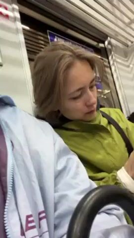 The video shows a woman sitting on a train, wearing a green jacket. She is cleaning her hands with a white tissue.  Another passenger, wearing a mask, is seated in the background. The train has horizontal overhead bars.  The lighting is typical of a subway car.