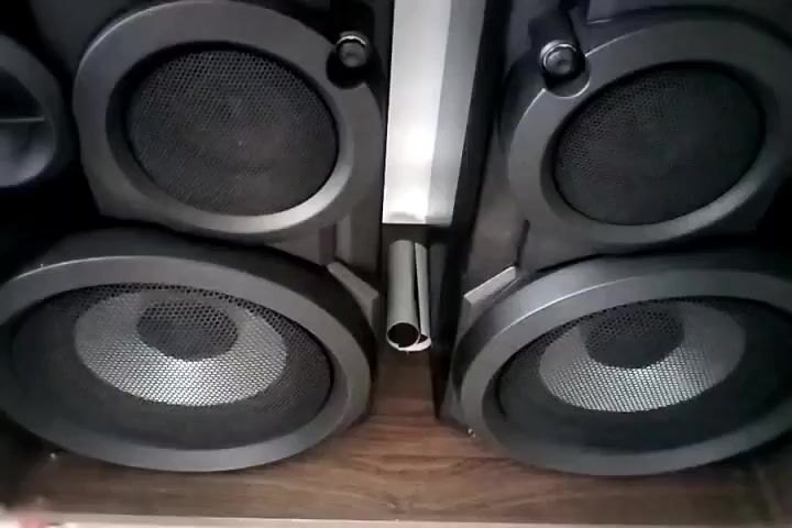 The video shows a close-up shot of four speakers. The speakers are black with silver cones. The speakers are arranged in two rows, with two speakers in each row. The speakers appear to be part of a stereo system. The background is a wooden surface. The lighting is dim. The audio consists of music.