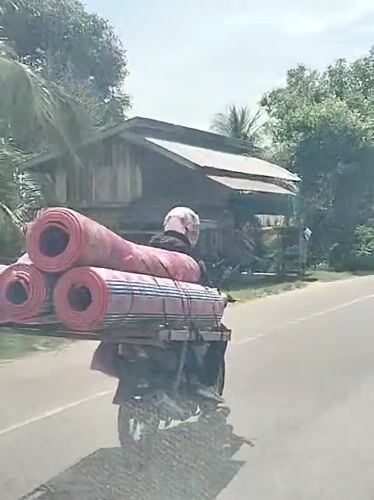 Motorcyclist transports rolled mats on Indonesian road