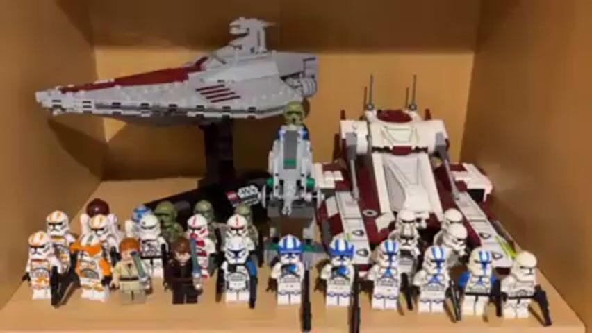 The video shows two shelves filled with Lego Star Wars sets and minifigures. The top shelf features a Venator-class Star Destroyer on a stand, an AT-TE walker, and a variety of Clone Trooper minifigures. The minifigures include members of the 501st, 212th, and Coruscant Guard legions, as well as Anakin Skywalker. The bottom shelf displays a Separatist army, including a Hailfire Droid, a Spider Droid, a Dwarf Spider Droid, and several Battle Droids. Both shelves are inside a wooden cabinet.