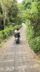 Two riders navigate scooter uphill on paved path in Sawan