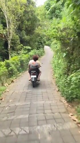 Two riders navigate scooter uphill on paved path in Sawan