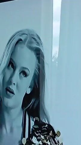 The video displays a close-up, black and white footage of a woman with blonde hair. She is looking towards the left of the frame with her mouth slightly open. She is wearing a dress with sequins on the shoulders. The background consists of vertical white blinds and a sliver of sky with trees visible. The footage appears to be of low resolution and possibly a recording of a screen.