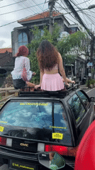 Two women sit on car roof in Bali