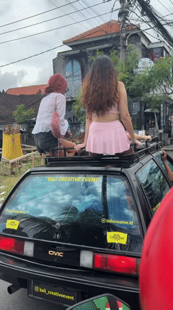 Two women sit on car roof in Bali