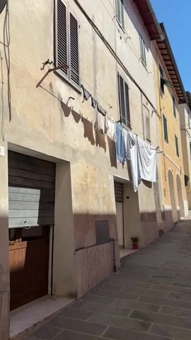 A narrow, cobblestone street curves uphill between two buildings with cream-colored facades and brown shutters on the windows. Laundry hangs on a line stretched between the buildings, flapping gently in the breeze. The sun casts sharp shadows on the street and the buildings. The scene appears to be in a European town.