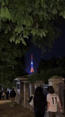 Pedestrians walk toward illuminated patriotic tower in Yerevan