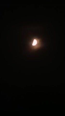 The video is a still image of a half-moon in a dark sky. The moon is partially obscured by clouds, giving it a hazy appearance. The sky is black, indicating nighttime. There are no other objects or people visible in the frame. The image is centered on the moon.