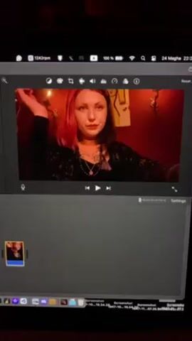 The video shows a computer screen with a screenshot of a person with pink-highlighted hair and a black shirt in a recording program. The background is red, with some decorations on the wall. There is a play button highlighted. The video shows the user using the video editing software.