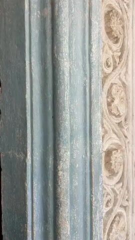 The video begins with a close-up of a wooden door frame, showing aged paint and wood grain. The perspective then shifts to a detailed view of a carved wooden door, featuring intricate patterns. Subsequently, the video pans to show a partially opened wooden door revealing the interior of a building. As the door opens further, the view expands to show people standing inside what appears to be a church or a similar grand hall. The hall has a high, arched ceiling with a starry pattern and a large, ornate chandelier hanging from it. In the foreground, two men are standing with their backs to the camera, facing the interior. Another woman is visible on the left. The scene conveys a sense of entering a historically significant or ornate place.