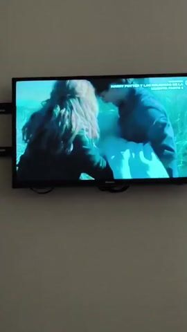 A Hisense television is displaying a scene from the movie "Harry Potter and the Deathly Hallows Part 2". The scene features Harry Potter and another figure, possibly Hermione Granger, interacting with a white object, possibly a shroud or a cloth. They are standing in a grassy area. The television is mounted on a light-colored wall.