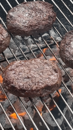 Burger patties grilling over charcoal flames captured in London