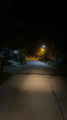 Motorcyclist travels illuminated road at night in Thong Sala