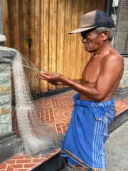 Elderly fisherman mends nets in early morning Kuta scene