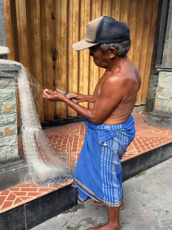 Elderly fisherman mends nets in early morning Kuta scene