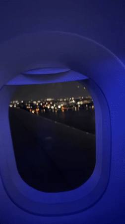 Night flight window view, wing lights glowing over New York