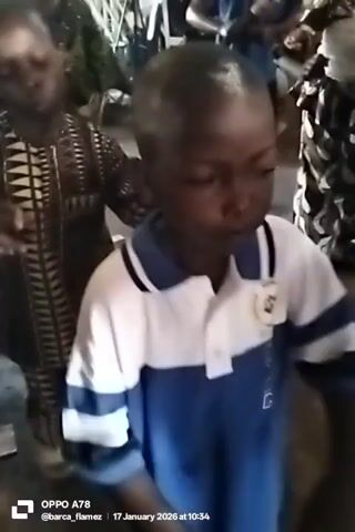 The video shows two boys dancing in what appears to be a gathering or celebration. One boy is wearing a blue and white collared shirt, while the other wears a patterned brown and black traditional garment. They are surrounded by other individuals, some of whom are wearing elaborately decorated outfits. The setting appears to be indoors, possibly a hall or a large room. The audio suggests there is music playing, possibly live, which they are dancing to.  The camera is slightly shaky, indicating it's handheld. A timestamp at the bottom of the frame indicates the date is 17 January 2026.