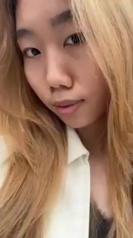 A young woman with fair skin and long blonde hair looks at the camera. She is wearing a white jacket. She shows a pink paper bag with "Luckin Coffee" and a cartoon bear printed on it. She then shows a long receipt. The background appears to be a city street.