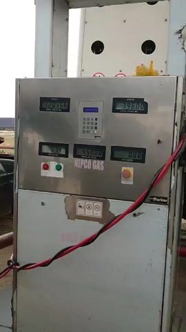 The video shows a NIPCO Gas fuel dispenser with digital displays showing total price and quantity for two arms. The price per standard cubic meter is displayed as 450.00. Next to the dispenser is a large white truck with the NNPCL logo and "MCC 071" printed on it. Two young men stand in front of the truck. The environment appears to be an outdoor industrial area.