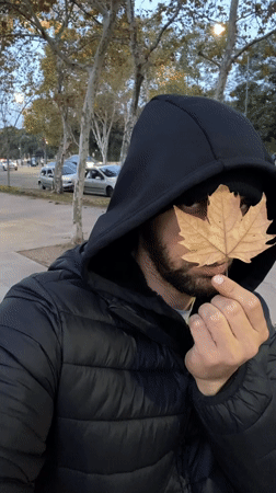 Man holds dried leaf over face on Buenos Aires sidewalk